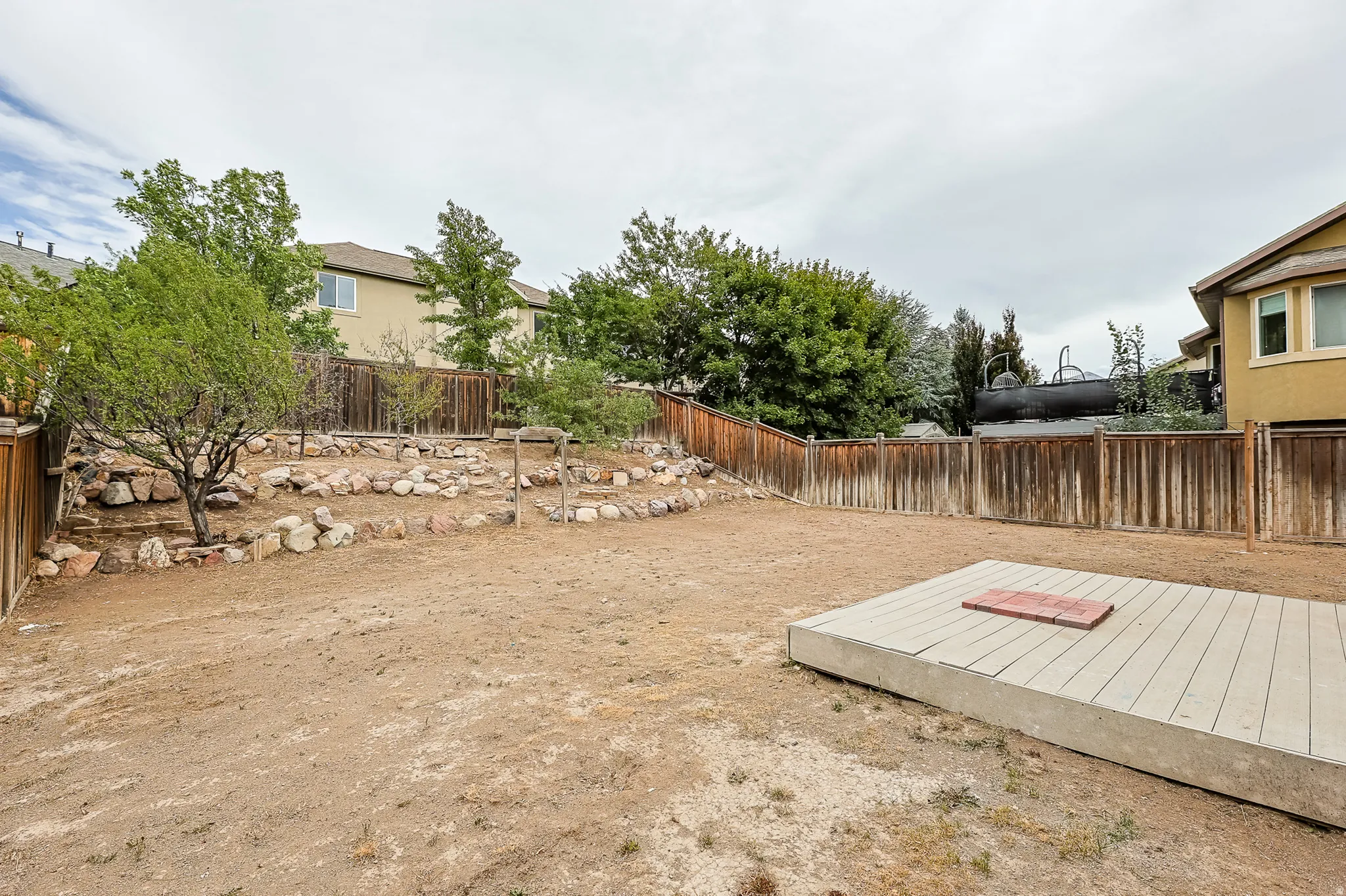 Expansive backyard featuring a tiered landscaping area with natural stone accents, wood privacy fencing, and a raised composite decking platform
