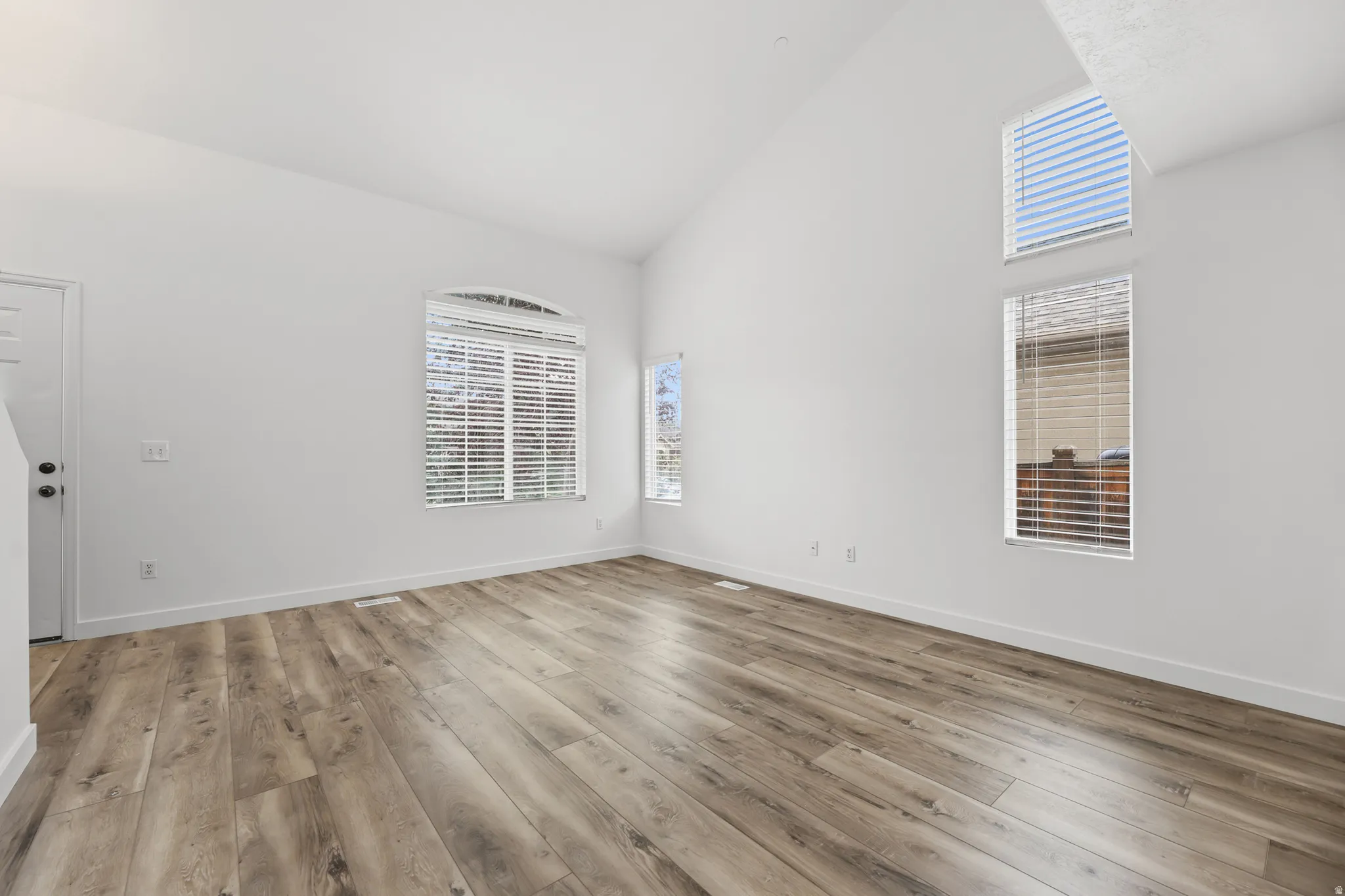 Vaulted ceiling with high windows, wood-finish flooring, white walls, and an arched window