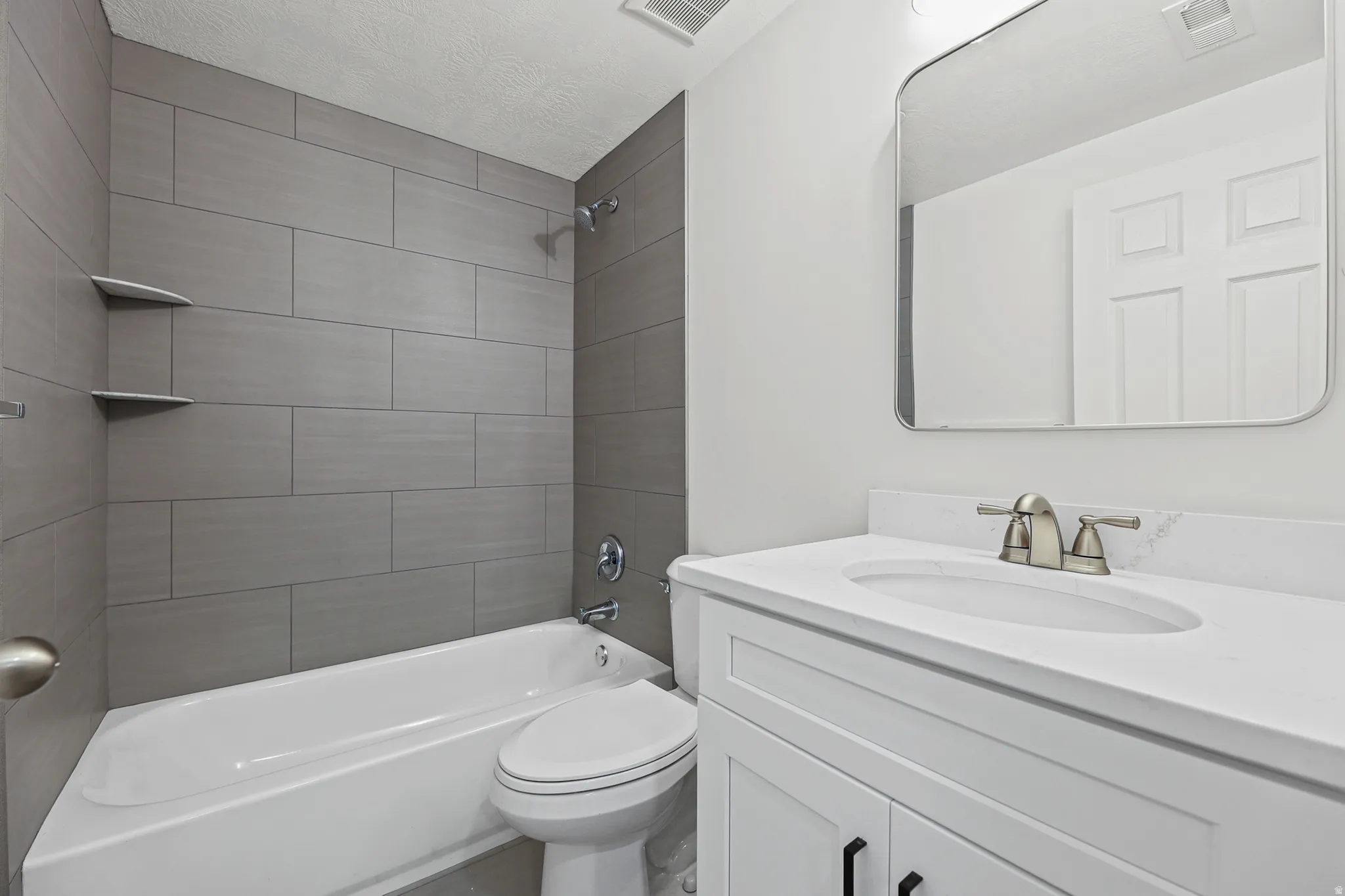White vanity with integrated sink and brushed nickel faucet, large wall mirror, and grey subway tile shower surround with built-in shelving
