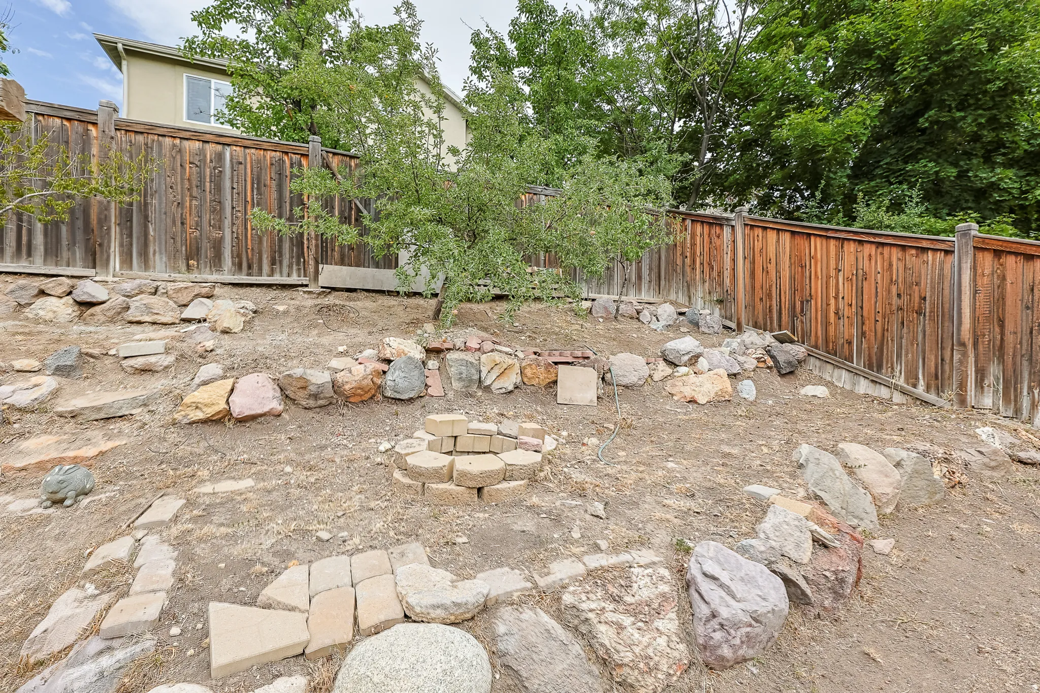 Terraced outdoor space featuring a stone-lined fire pit, wood privacy fencing, and mature trees