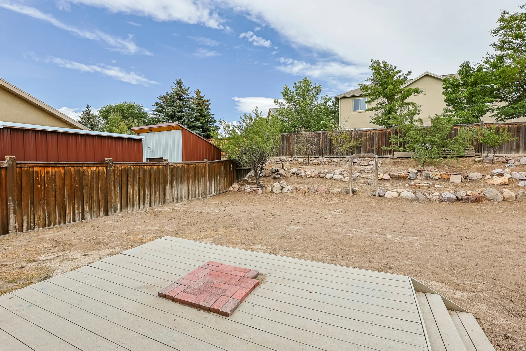 Fenced backyard with an elevated deck, brick paver accent, and a terraced rock garden