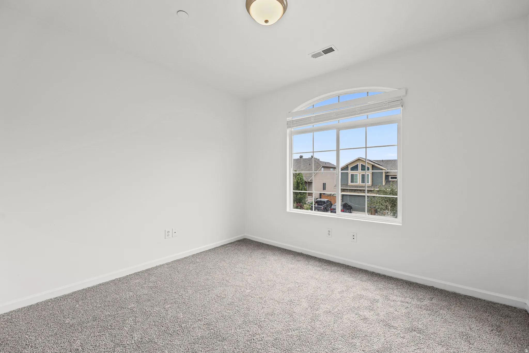 Room featuring a large arched window with horizontal blinds, grey carpet, and a flush mount ceiling light