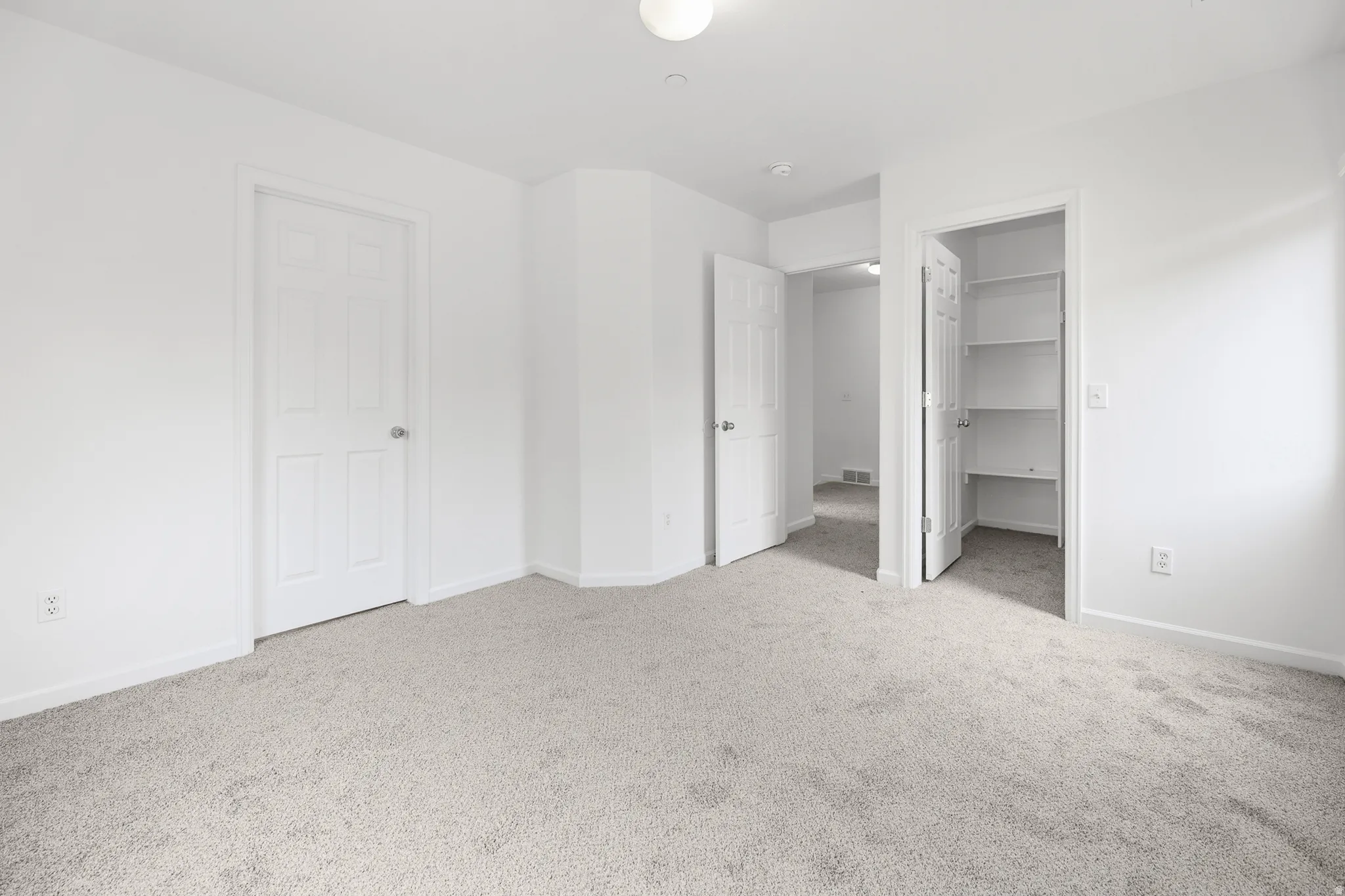 Carpeted room with white walls, multiple doorways, and an integrated storage closet with shelving