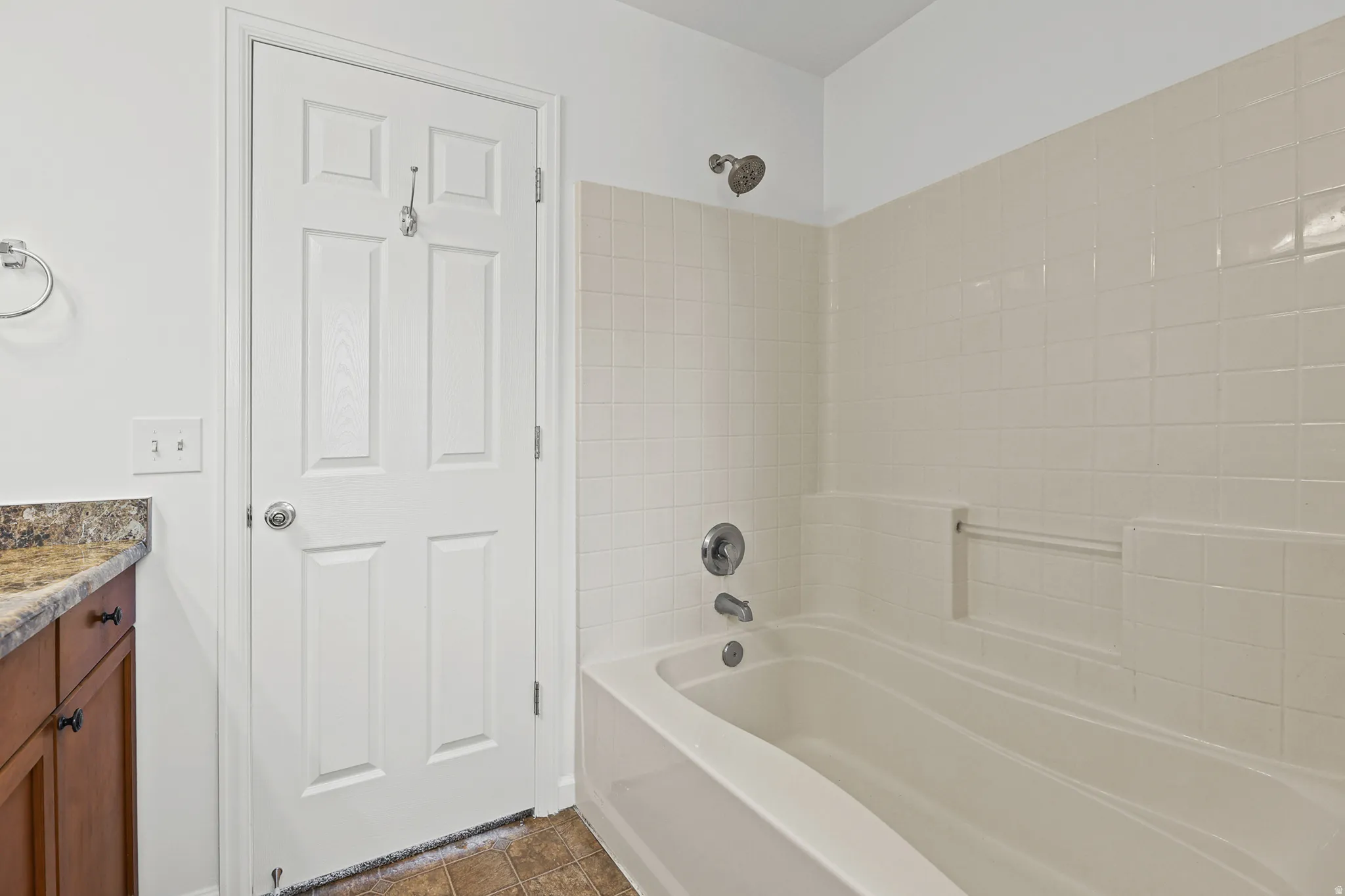 Bathtub with shower fixture, tiled surround, and a vanity featuring a stone-finish countertop