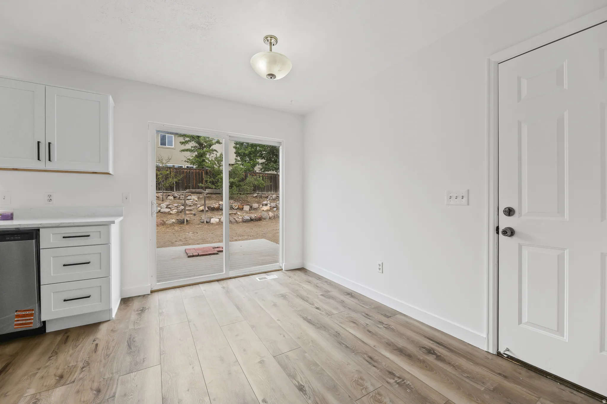 Wood-finish flooring, white cabinetry with dark hardware, white countertops, stainless steel appliance, and glass sliding door