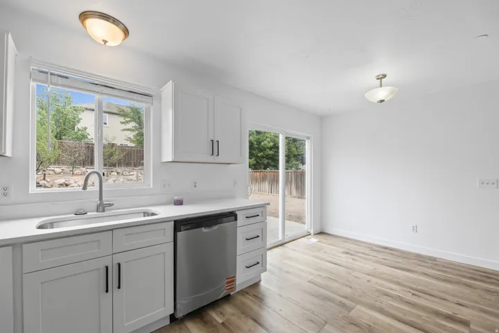 White shaker cabinetry, stainless steel dishwasher, single basin sink, white countertops, and wood-finish flooring