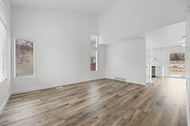 Vaulted ceilings, wood-finish flooring, multiple windows with blinds, white painted walls, and a white paneled door