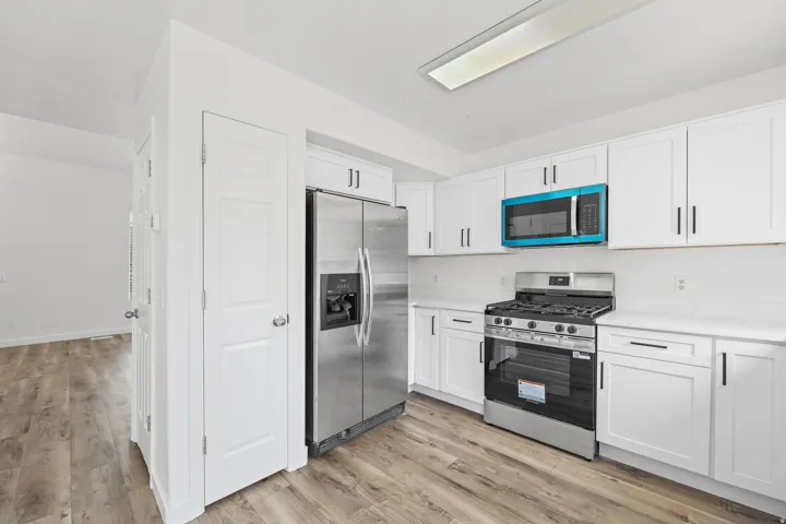 Contemporary kitchen featuring white cabinetry, stainless steel appliances, white countertops, and wood-finish flooring