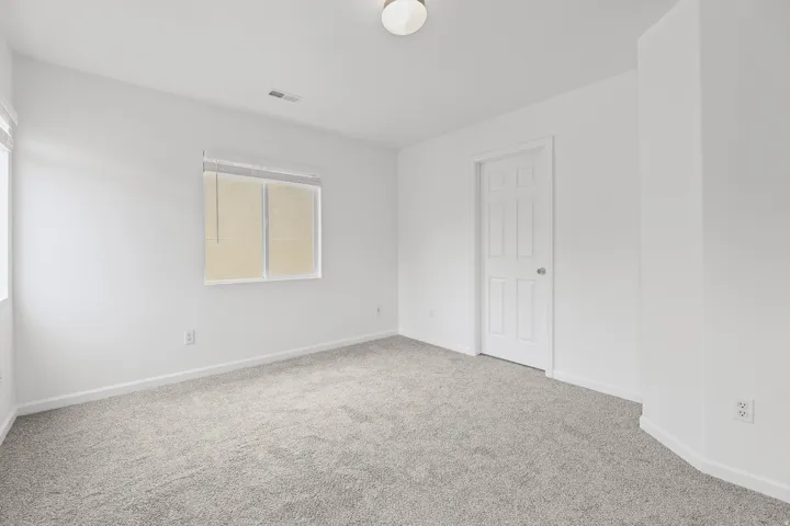 Neutral-toned carpeting, white painted walls, and a single window with blinds