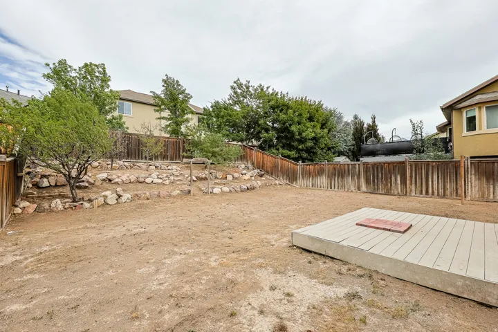 Expansive backyard featuring a tiered landscaping area with natural stone accents, wood privacy fencing, and a raised composite decking platform