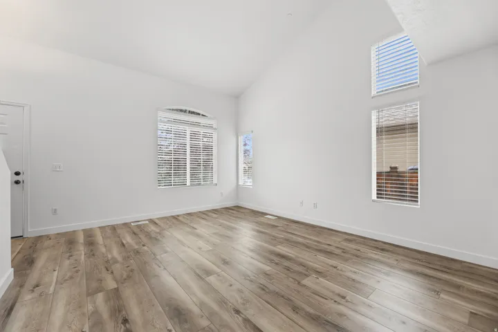 Vaulted ceiling with high windows, wood-finish flooring, white walls, and an arched window