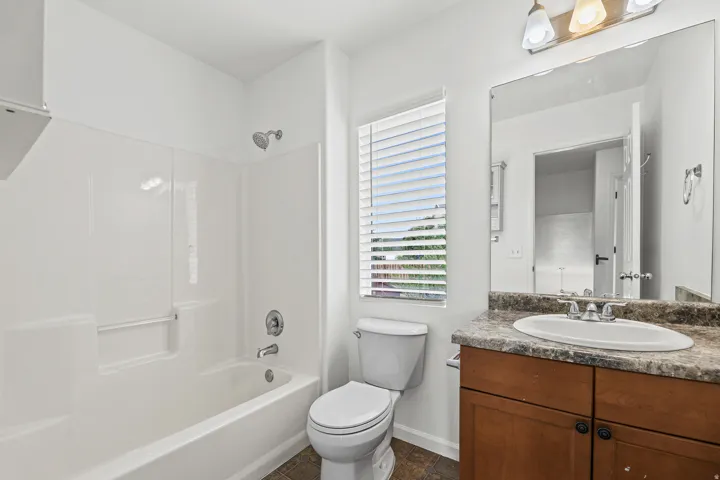 Built-in bathtub with shower, wood-finish vanity with an integrated sink, and an expansive mirror