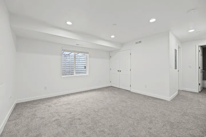 Recessed lighting, light gray carpet flooring, white walls, double bi-fold closet doors, and an egress window