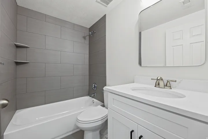 White vanity with integrated sink and brushed nickel faucet, large wall mirror, and grey subway tile shower surround with built-in shelving