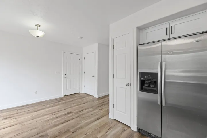 Stainless steel side-by-side refrigerator, white flat-panel cabinetry with dark hardware, and wood-finish flooring