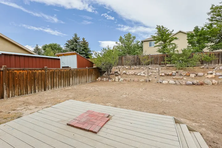 Fenced backyard with an elevated deck, brick paver accent, and a terraced rock garden