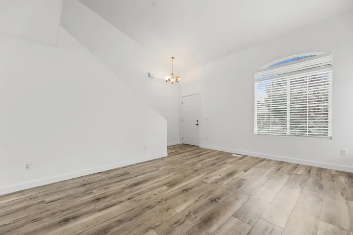 Wood-finish flooring, white walls, arched window with blinds, and an overhead light fixture