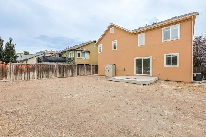 Expansive rear yard featuring a concrete patio, wood fence, and stucco exterior