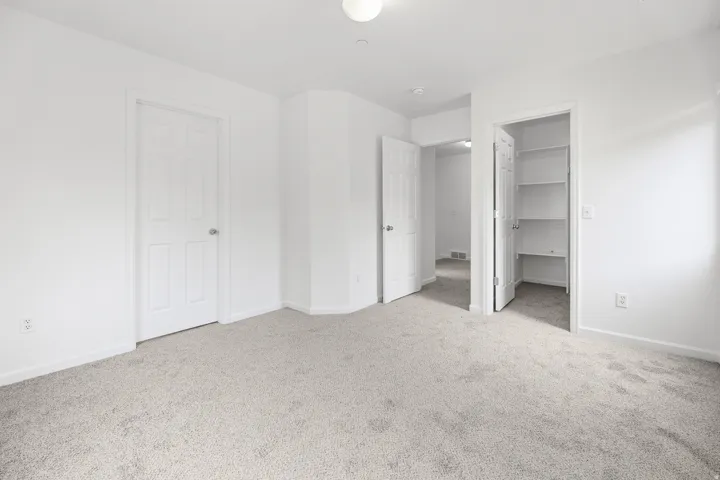 Carpeted room with white walls, multiple doorways, and an integrated storage closet with shelving