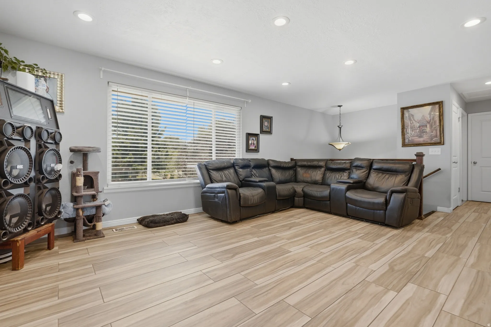Recessed lighting, wood-finish flooring, ample natural light from a large window, light gray wall color, and a built-in banister
