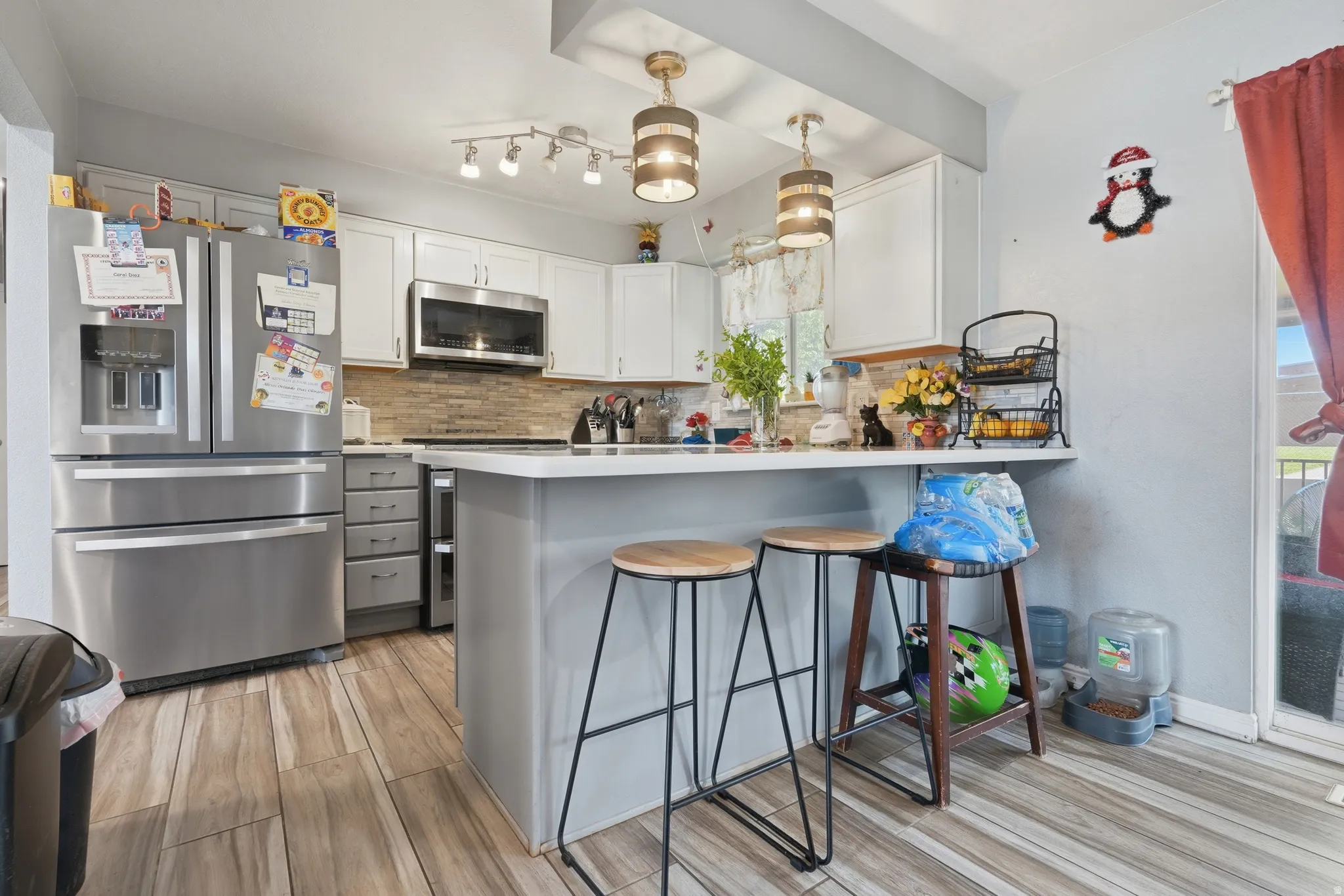 Kitchen featuring wood-finish flooring, white cabinetry, a large stainless steel refrigerator, and a breakfast bar with pendant lighting