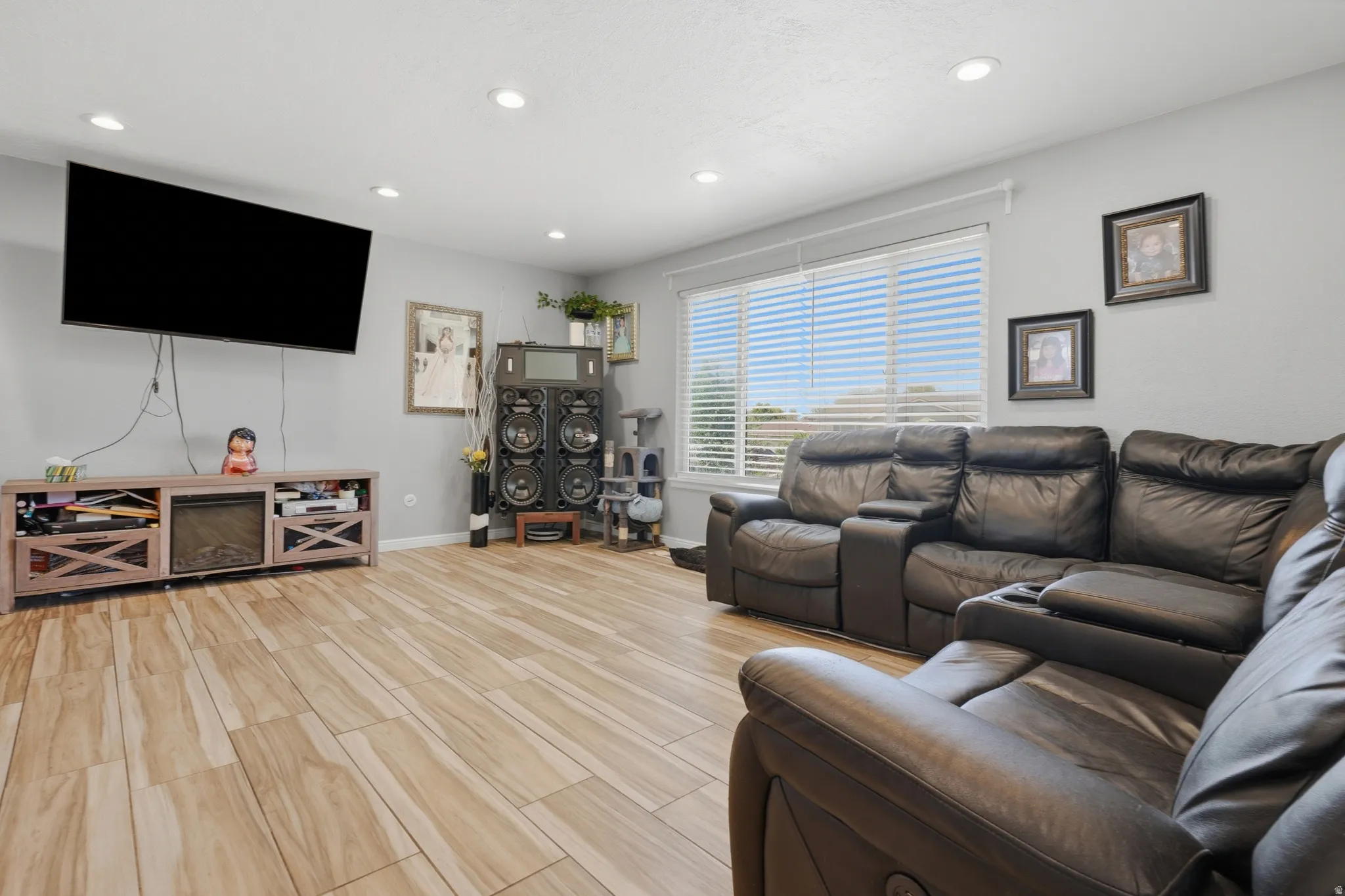 Wood-finish flooring, recessed ceiling lighting, light gray wall color, and a large window with blinds