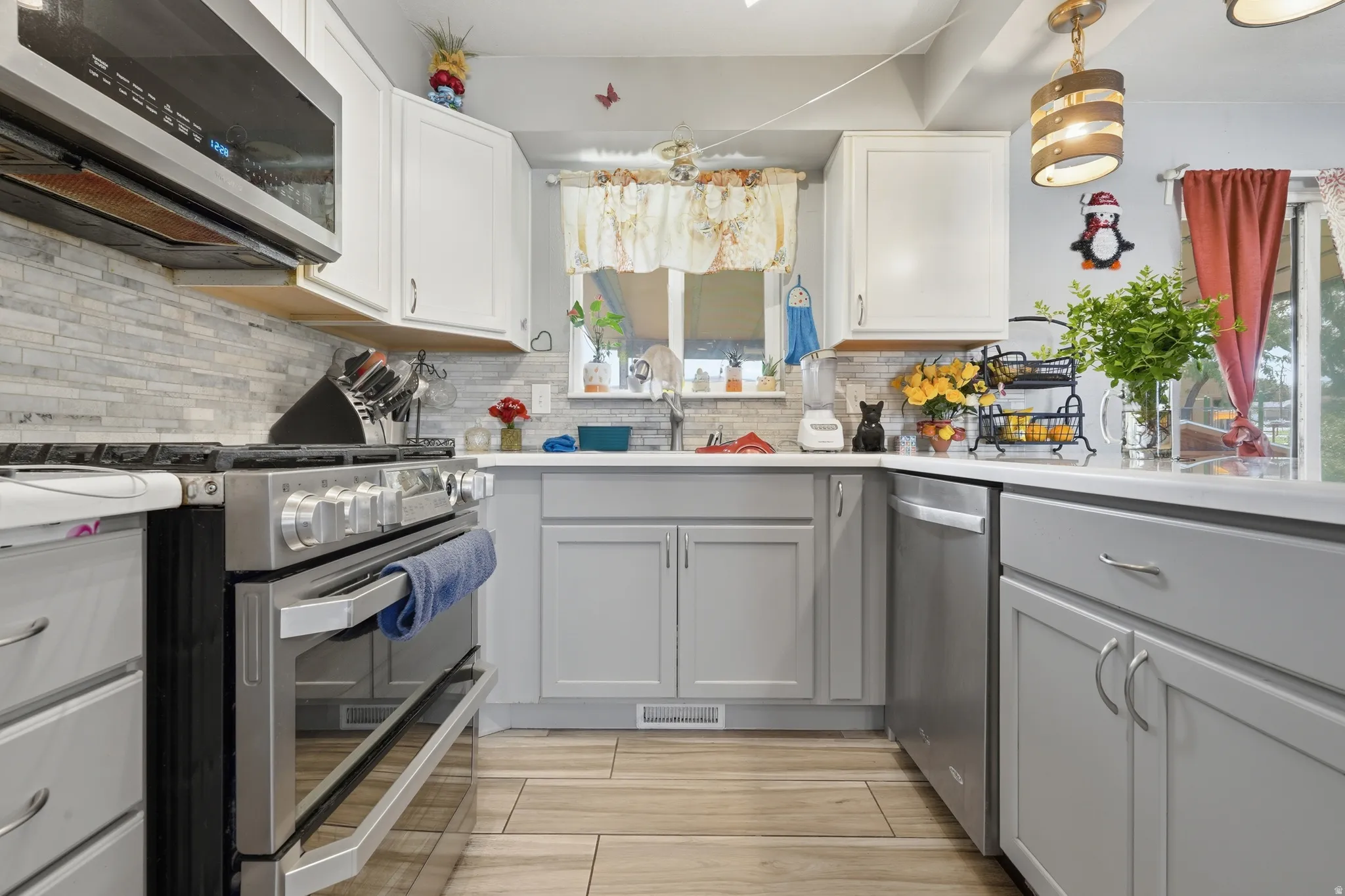 Kitchen featuring stainless steel appliances, light gray lower cabinetry, white upper cabinetry, and a subway tile backsplash