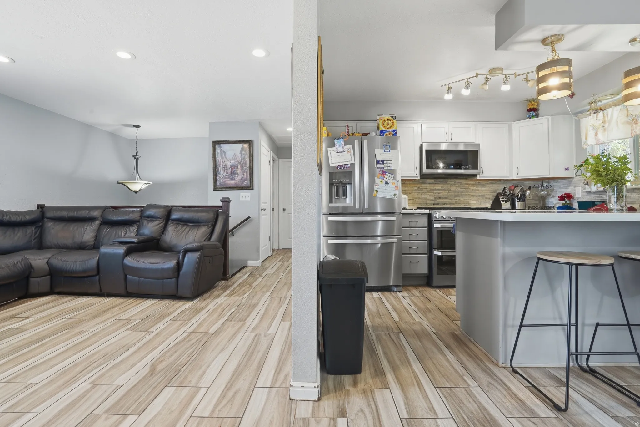 Recessed lighting, wood-finish flooring, white cabinetry, stainless steel appliances, and a tiled backsplash