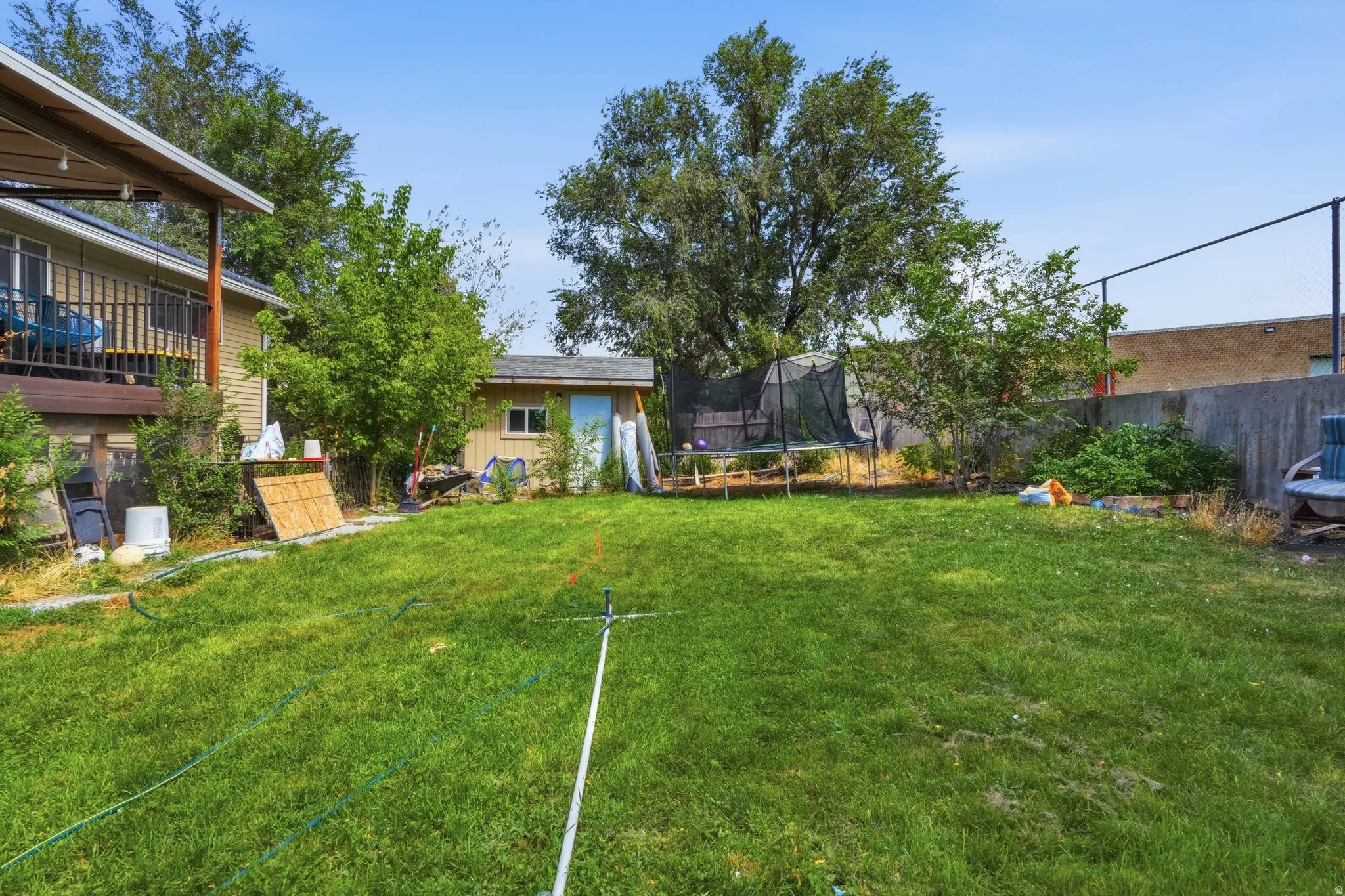 Expansive grassy yard featuring mature trees, a wooden storage shed, and a privacy fence