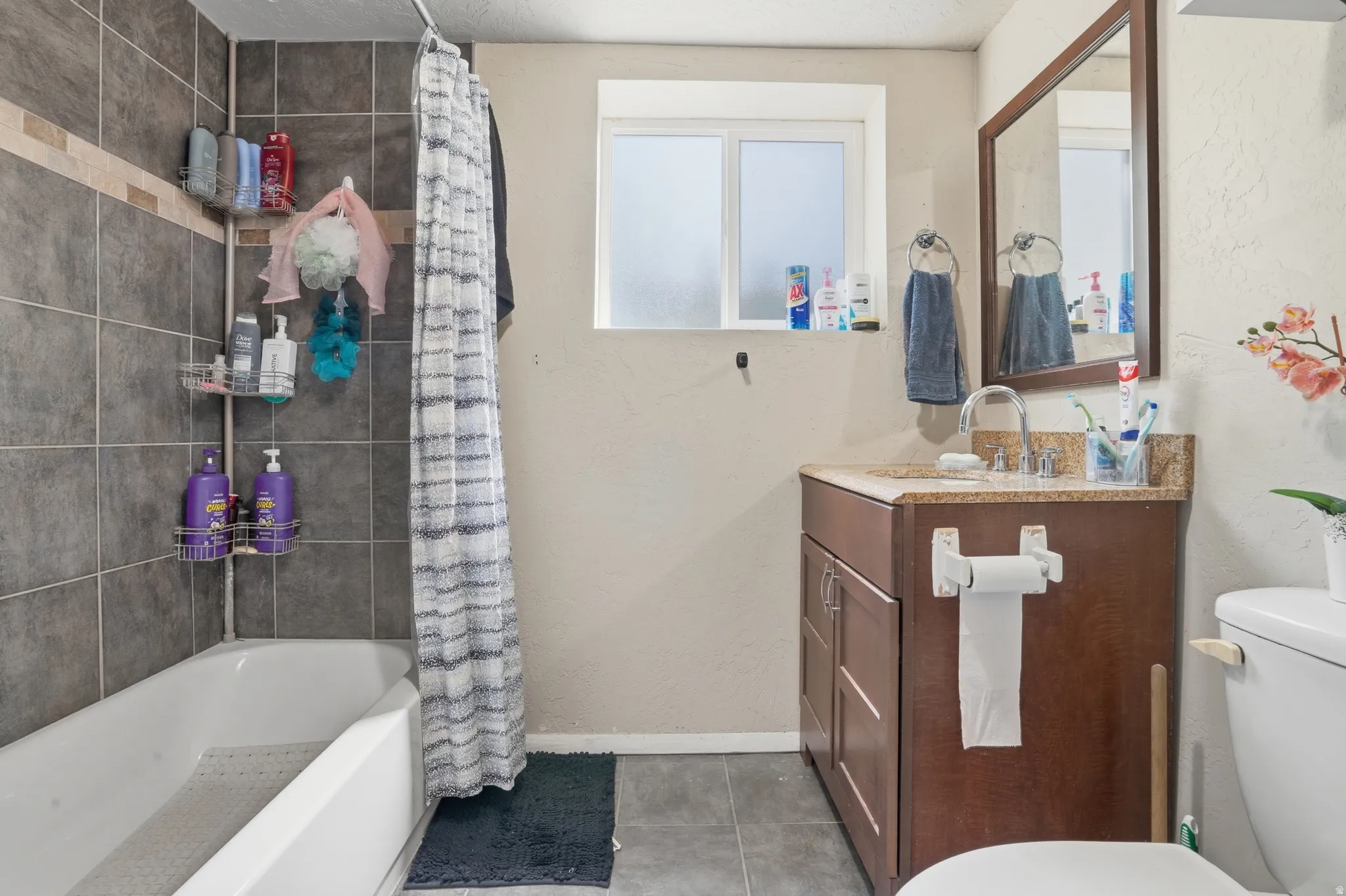 Built-in bathtub with subway tile surround, single-pane window, vanity with integrated sink and storage, framed mirror, and toilet