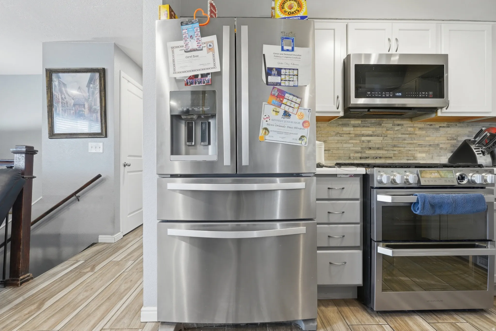Stainless steel appliances, wood-finish flooring, white cabinetry, textured tile backsplash, and light gray wall paint
