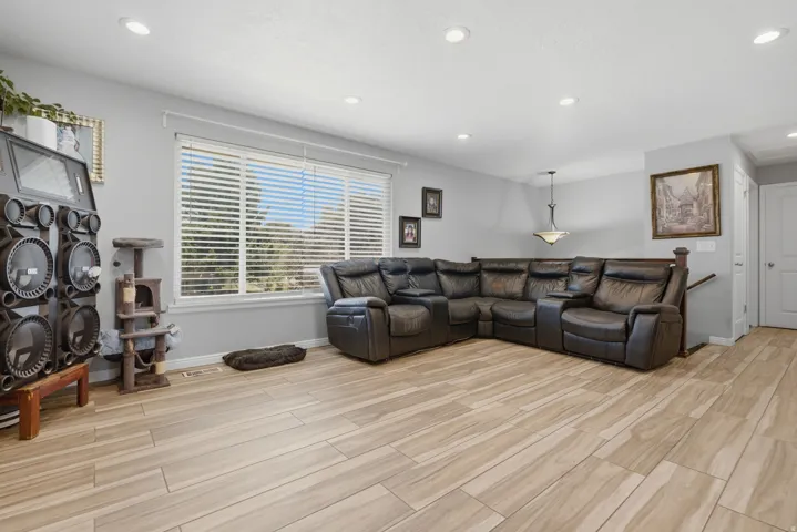 Recessed lighting, wood-finish flooring, ample natural light from a large window, light gray wall color, and a built-in banister