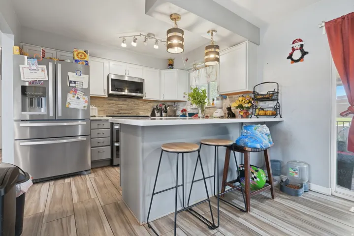 Kitchen featuring wood-finish flooring, white cabinetry, a large stainless steel refrigerator, and a breakfast bar with pendant lighting