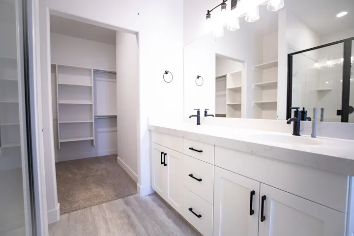 Primary bathroom with dual sinks, painted white wood cabinets, quartz slab countertops, walk-in shower and spacious walk-in closet as part of primary suite.