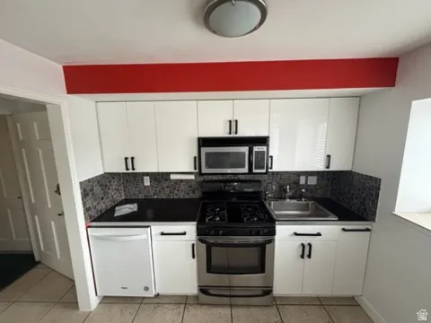 Stainless steel appliances, built-in microwave, white cabinetry, dark countertops, and mosaic tile backsplash