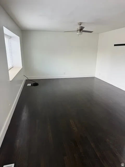 Spacious room with dark wood-finish flooring, white walls, and a ceiling fan with integrated lighting