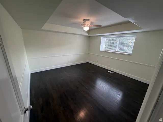 Tray ceiling featuring a ceiling fan, dark wood-finish flooring, and crown molding