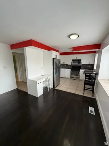 Dark wood-finish flooring, white cabinetry, stainless steel appliances, and integrated desk space