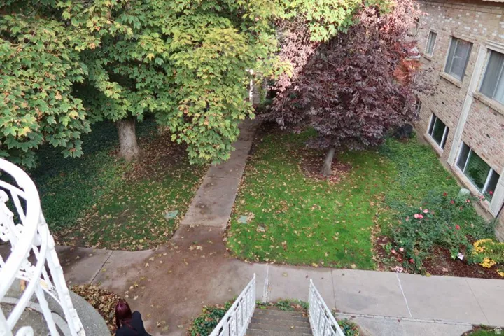 Manicured lawn with mature trees and shrubbery, concrete pathways, and a brick exterior building