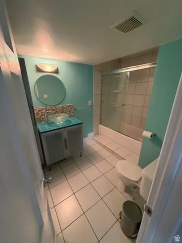 Bathroom with a glass vessel sink, tiled countertop, under-sink cabinetry, and a shower-tub combination with a glass enclosure