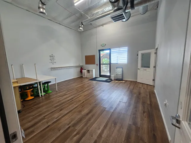 Spacious room featuring wood-finish flooring, exposed ductwork, a large window with blinds, and white walls