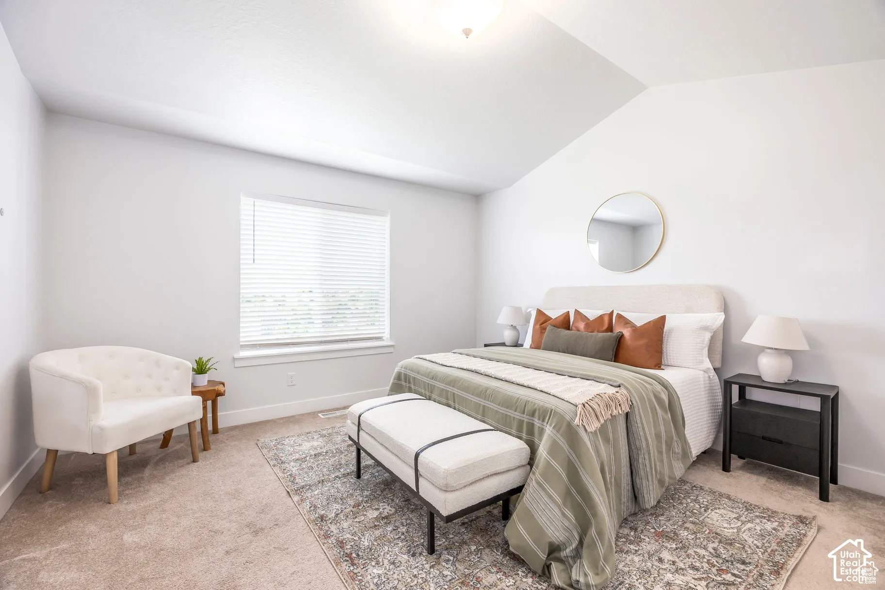 Vaulted ceiling, neutral wall tones, carpeted flooring, large window with blinds, and a built-in light fixture