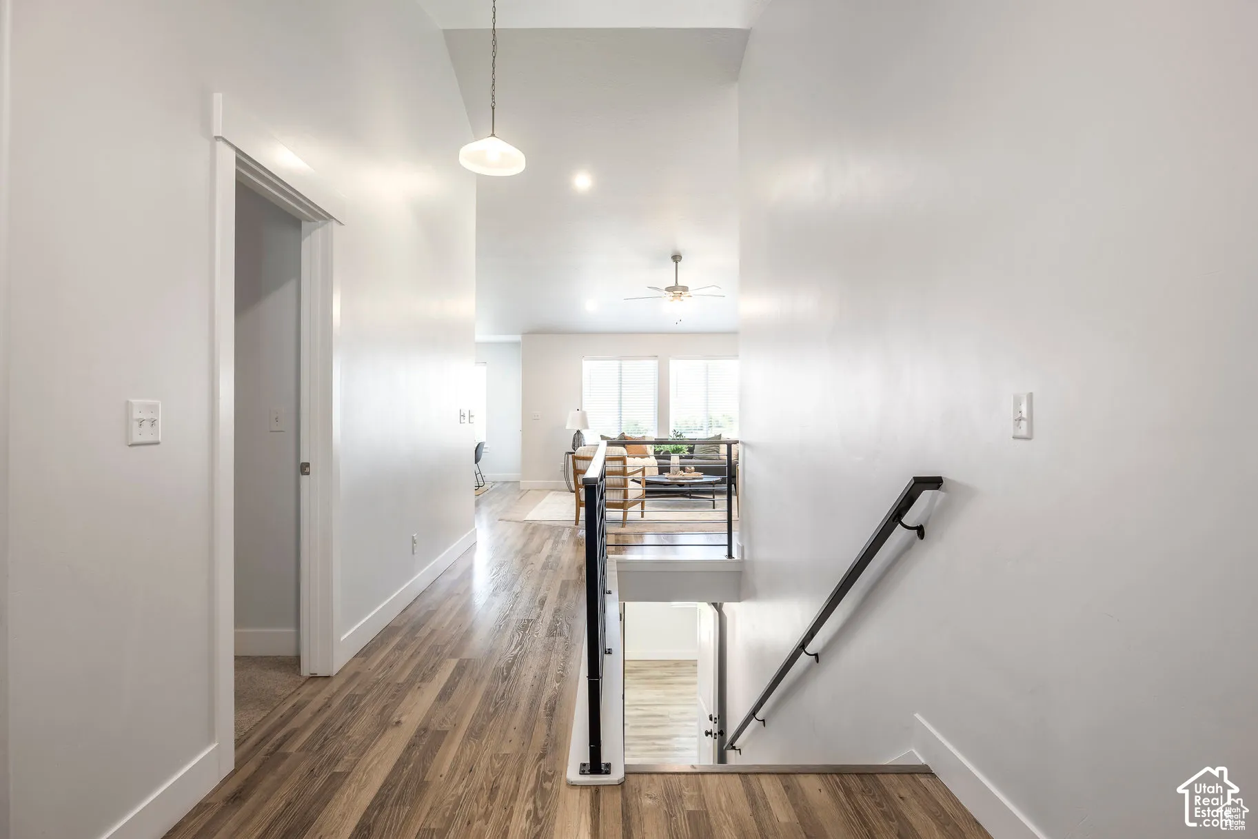 Wood-finish flooring throughout, modern pendant lighting, recessed ceiling lights, and a white painted railing with a dark handrail