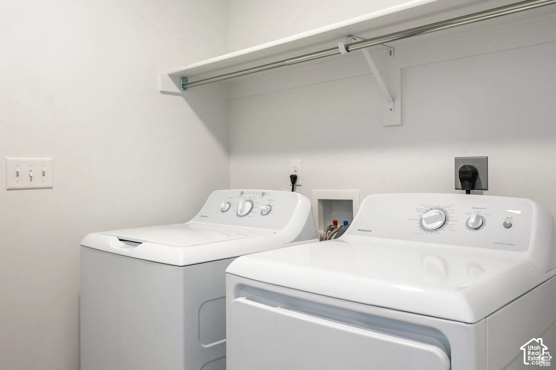 Integrated laundry area featuring white walls, a built-in shelf, and an overhead hanging rod