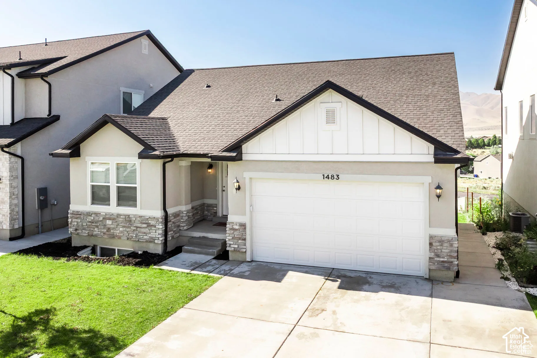 Contemporary exterior with a two-car garage, stone and stucco facade, dark shingle roof, and a concrete driveway