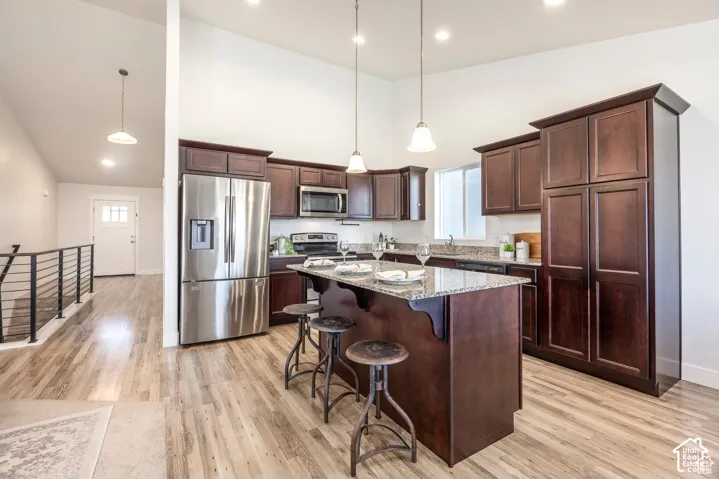 Kitchen featuring wood-finish flooring, vaulted ceilings, recessed lighting, a kitchen island with stone-finish countertops, and stainless steel appliances
