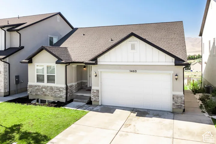 Contemporary exterior with a two-car garage, stone and stucco facade, dark shingle roof, and a concrete driveway
