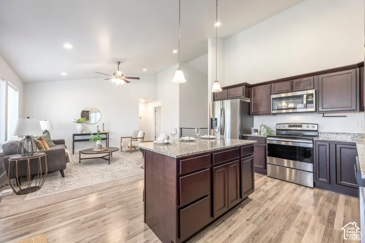 Kitchen island with stone-look countertop, wood-finish flooring, recessed lighting, stainless steel appliances, and dark wood cabinetry