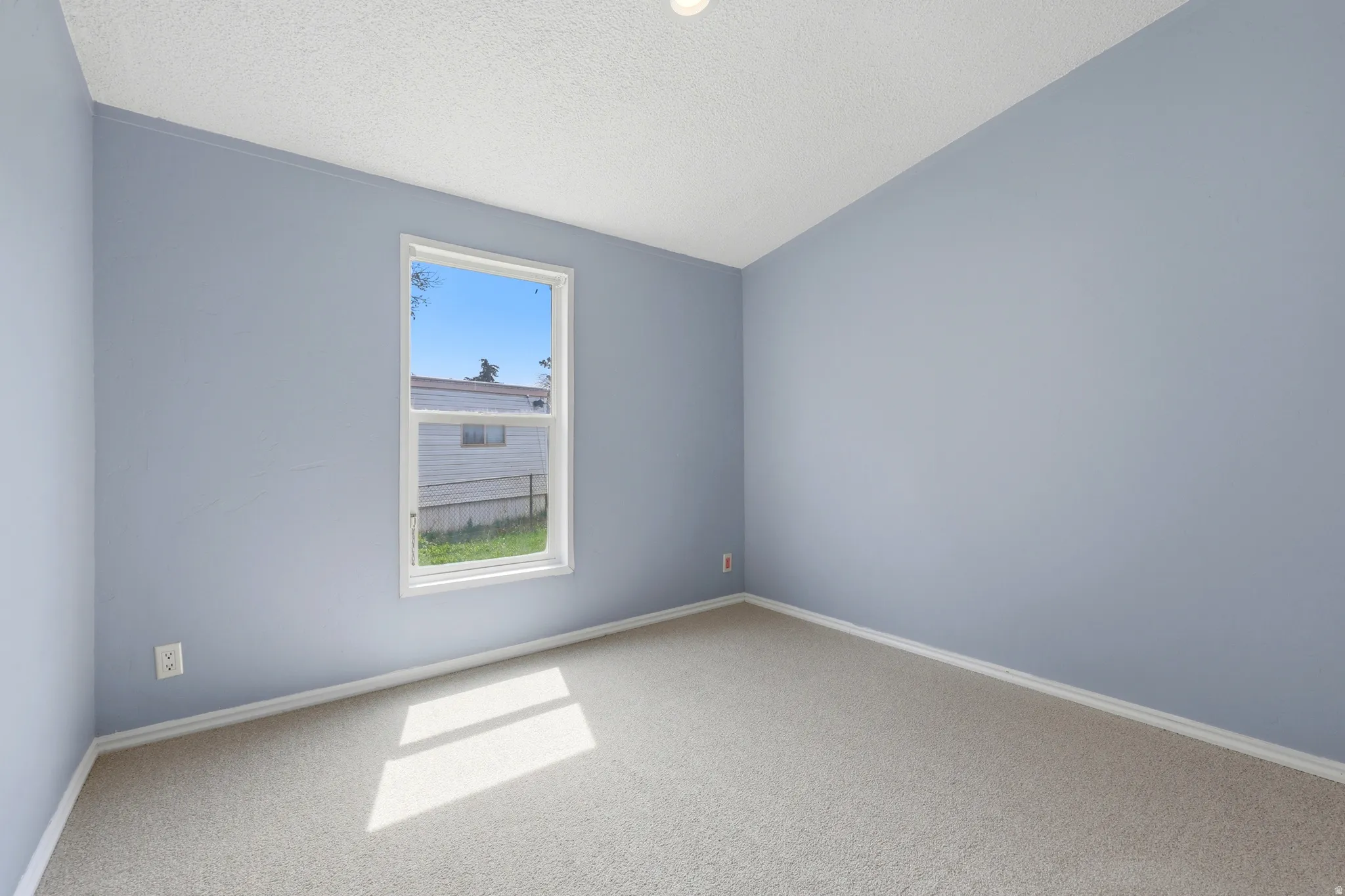 Neutral-toned carpeting, light blue wall paint, single window, and a textured ceiling