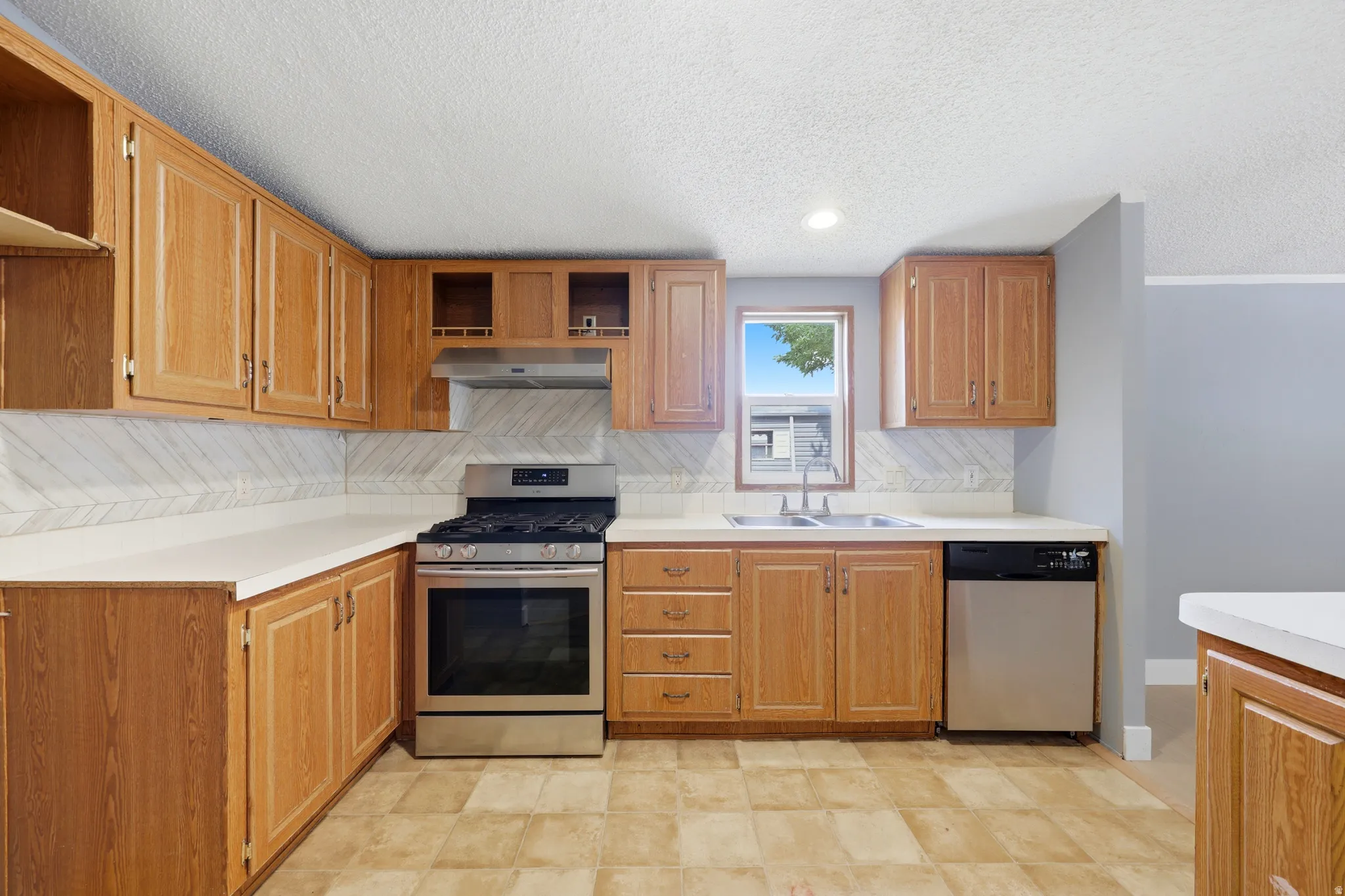 Full kitchen with wood cabinetry, stainless steel range, stainless steel dishwasher, and a double basin sink